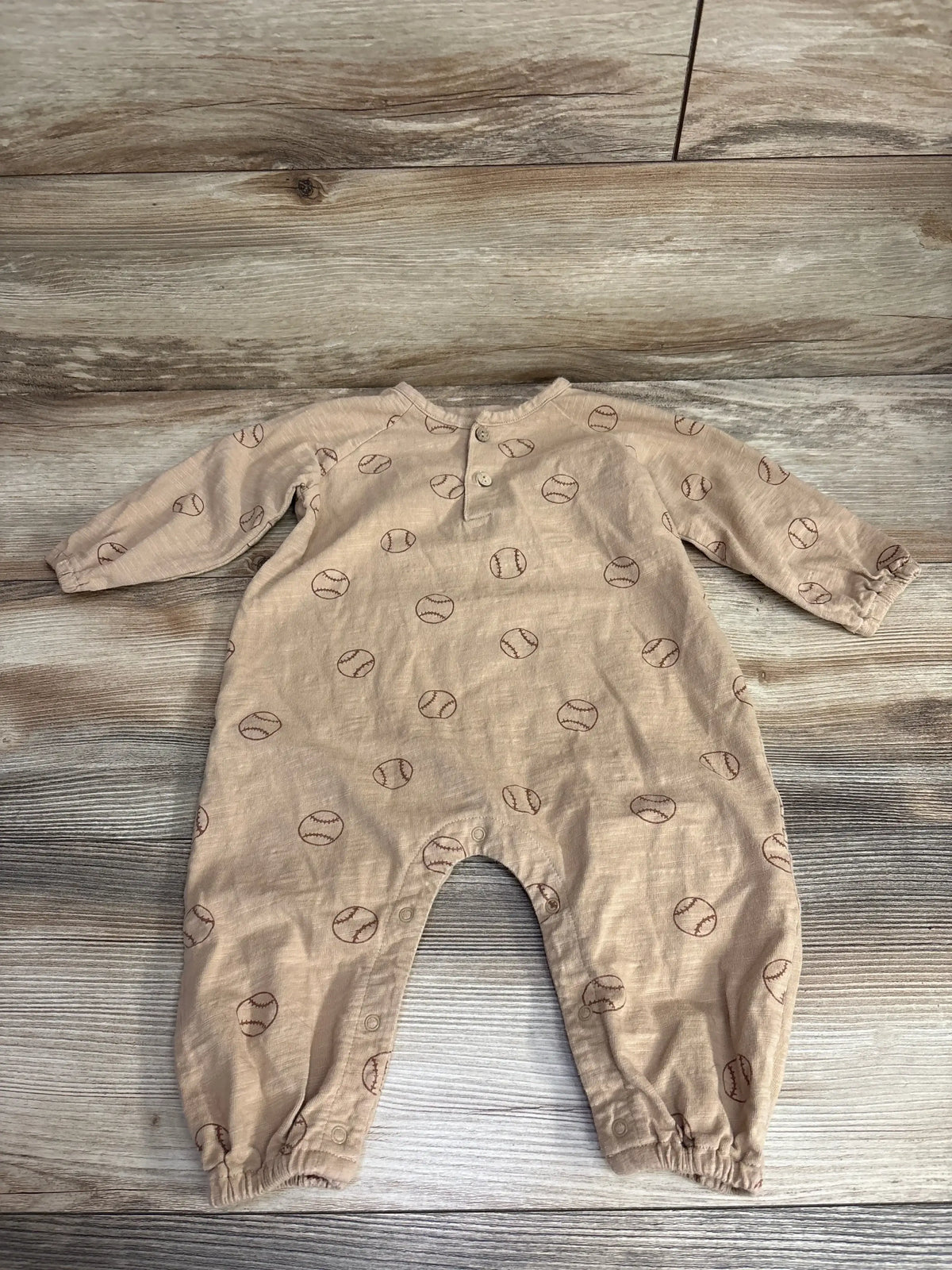 Beige baby romper with long sleeves and brown baseball print, laid flat on wood floor