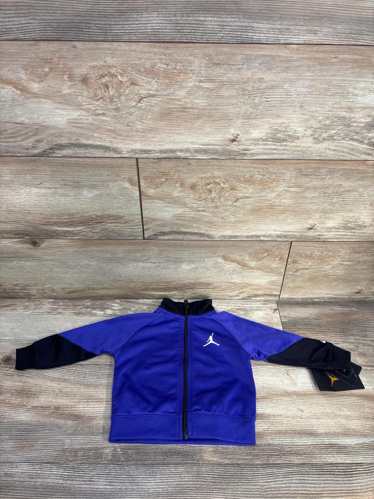 Front view of Jordan full-zip track jacket showcasing purple body, black sleeves, and white Jumpman logo on a wood-look background