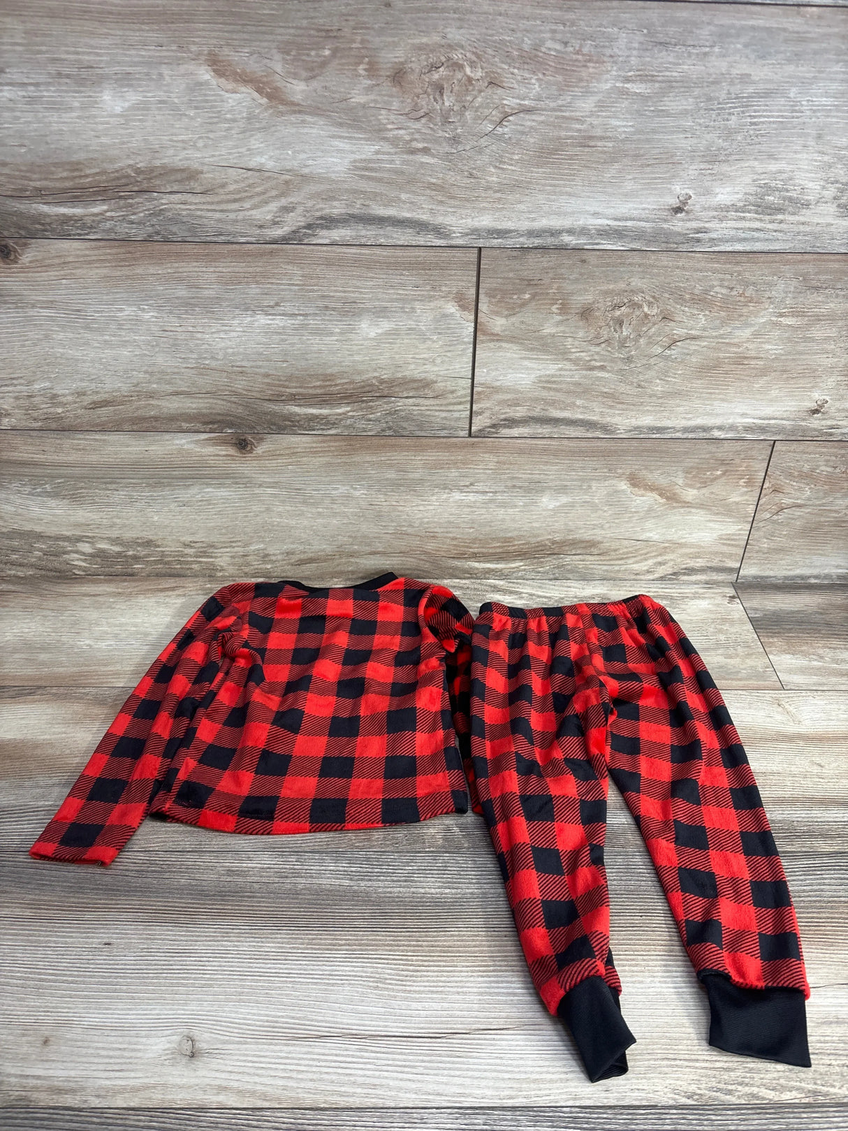 Red and black plaid kids pajama set with long sleeves and pants on wood floor