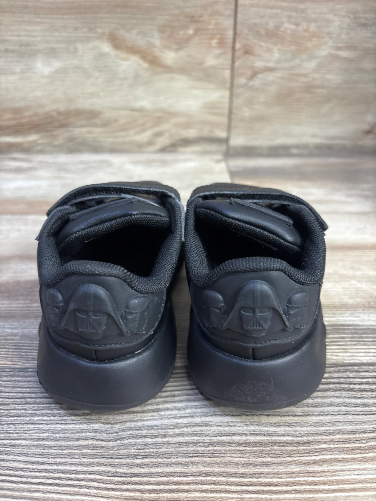 Rear view of Adidas x Star Wars toddler sneakers size 9.5C showing molded Darth Vader heel detail and double strap closures on wood floor background