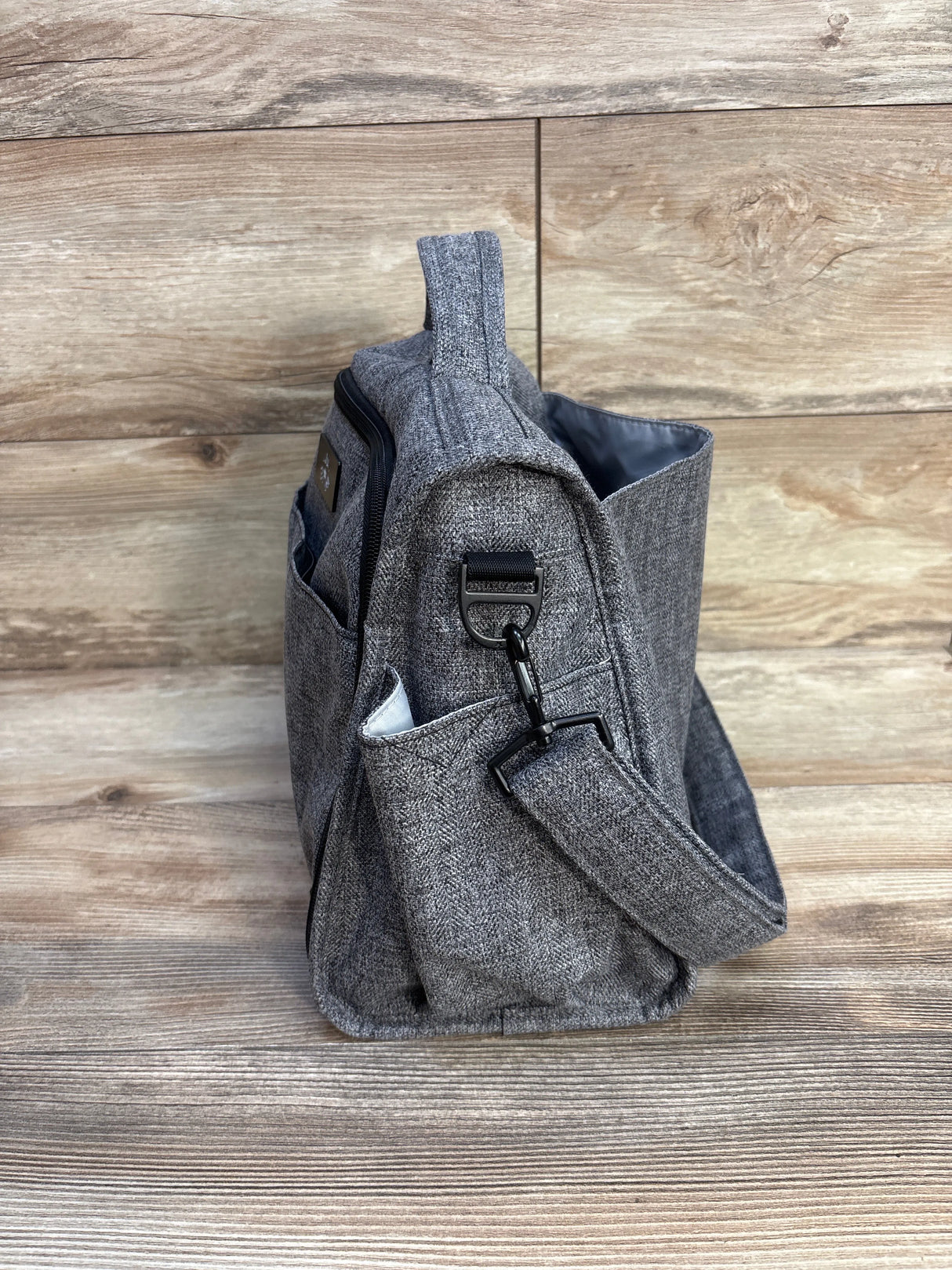 Gray fabric shoulder bag with side pocket and clasp on wood floor background