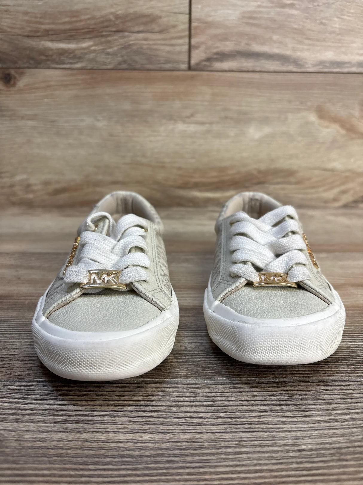 Front view of Michael Kors Court toddler sneakers in beige showing gold MK lace accents and textured canvas upper on wood floor