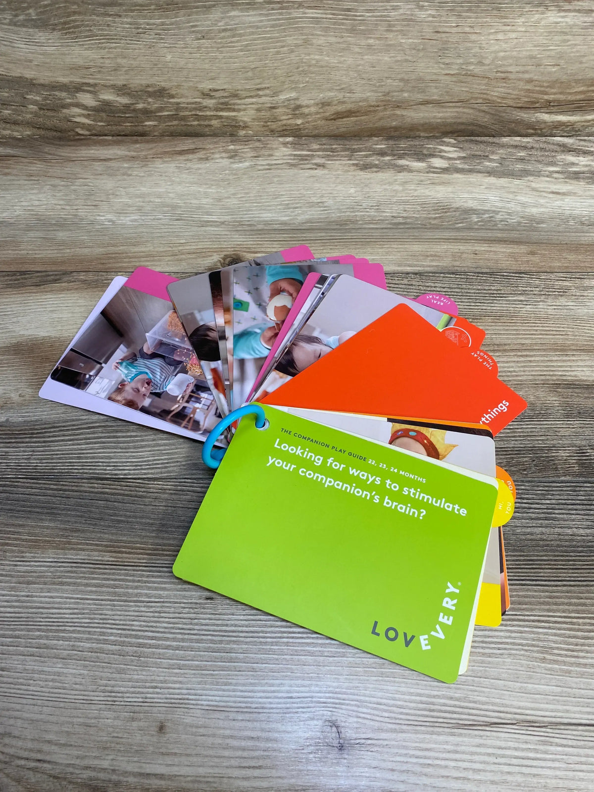 Lovevery play guide activity cards with photos, colorful tabs, on wooden table