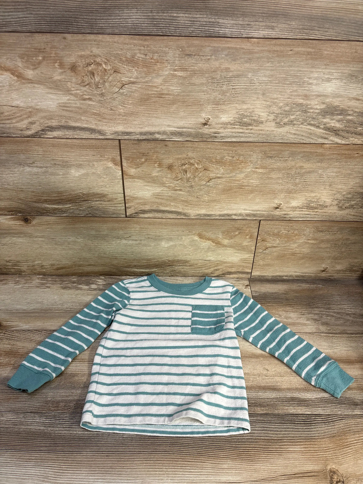 Front view of Cat & Jack teal striped pocket shirt with long sleeves and chest pocket on wood background