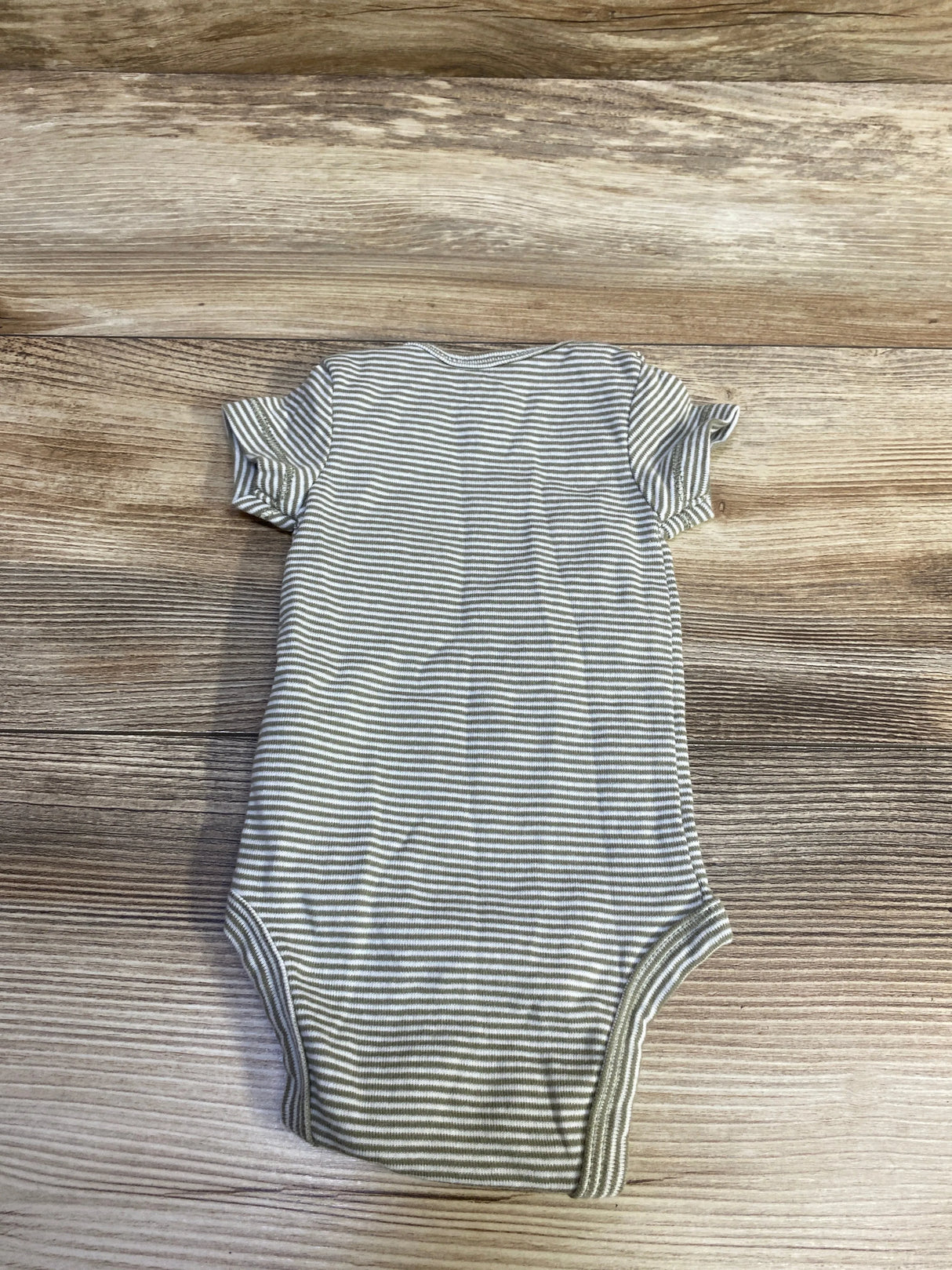 Back view of Carter’s newborn bodysuit in green and white stripes showing short sleeves and leg snaps on wood background