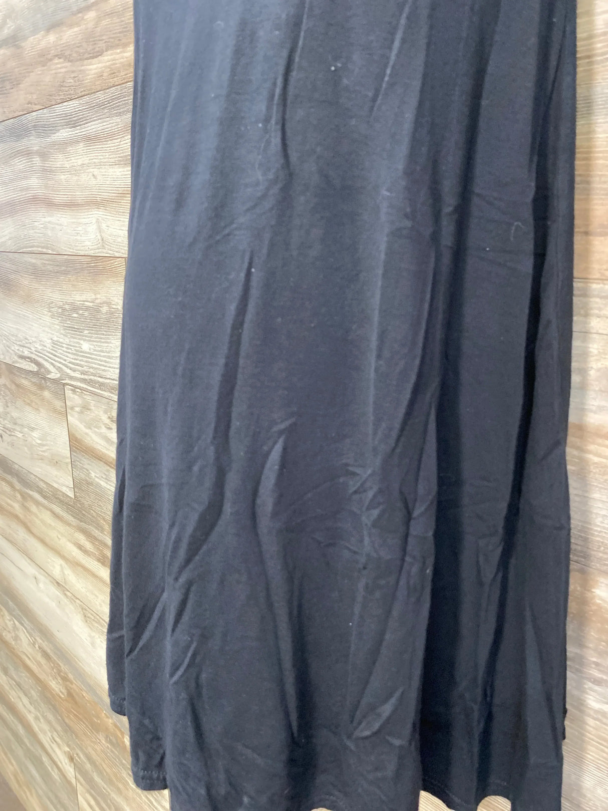 Close-up front of Boohoo black maternity swing top showing lower hem and fabric drape against wood wall