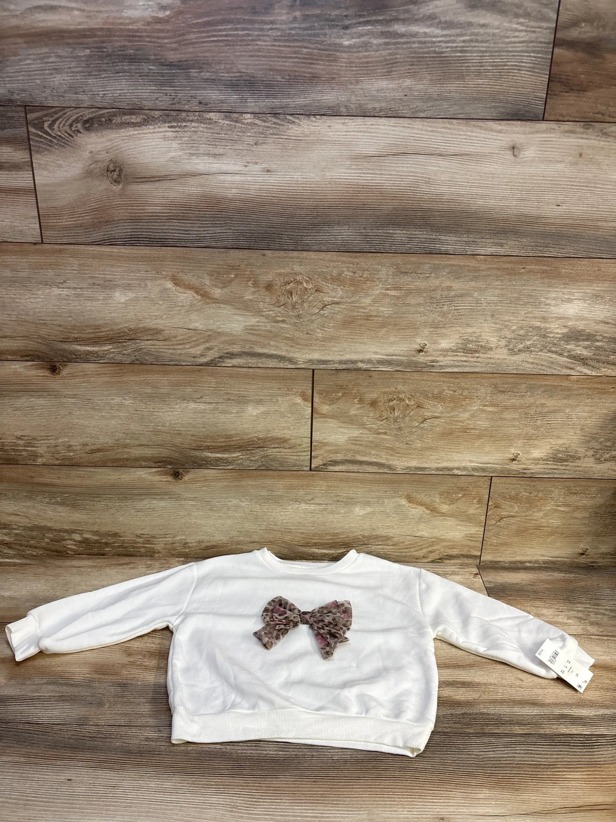 White Disney Junior Minnie Mouse bow sweatshirt for toddlers, size 5T, on a wood background.