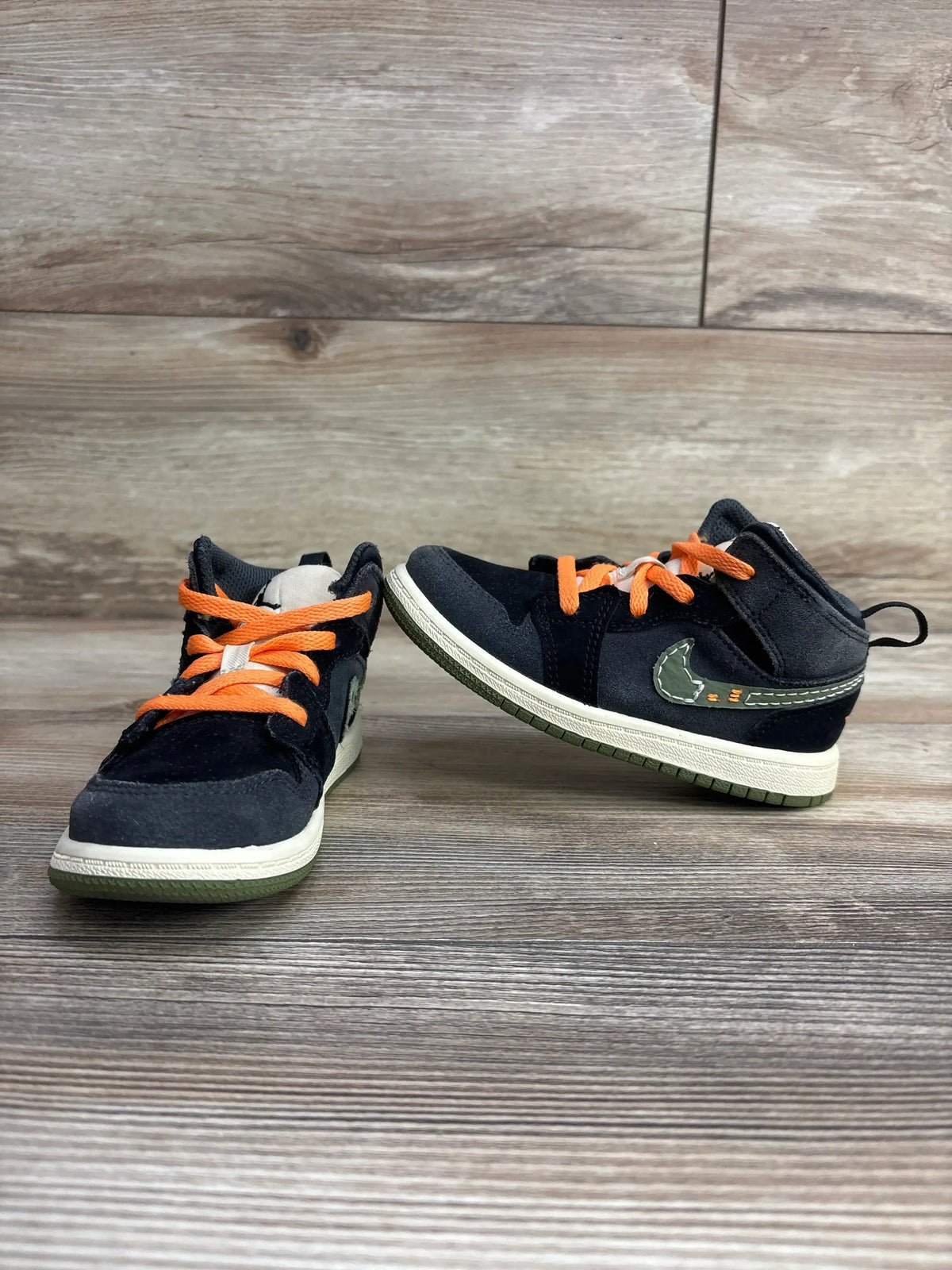Kids black sneakers with orange laces and green accents on wood background