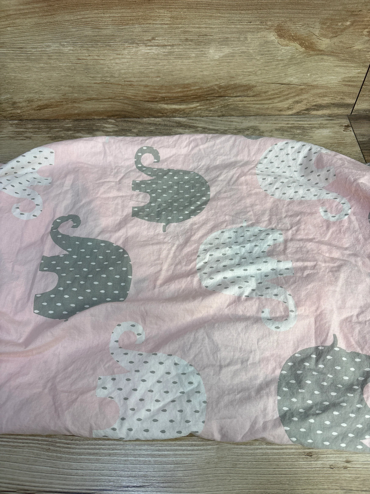 Top down view of NoJo fitted crib sheet showing gray and white polka dot elephant pattern on pink background on wood floor