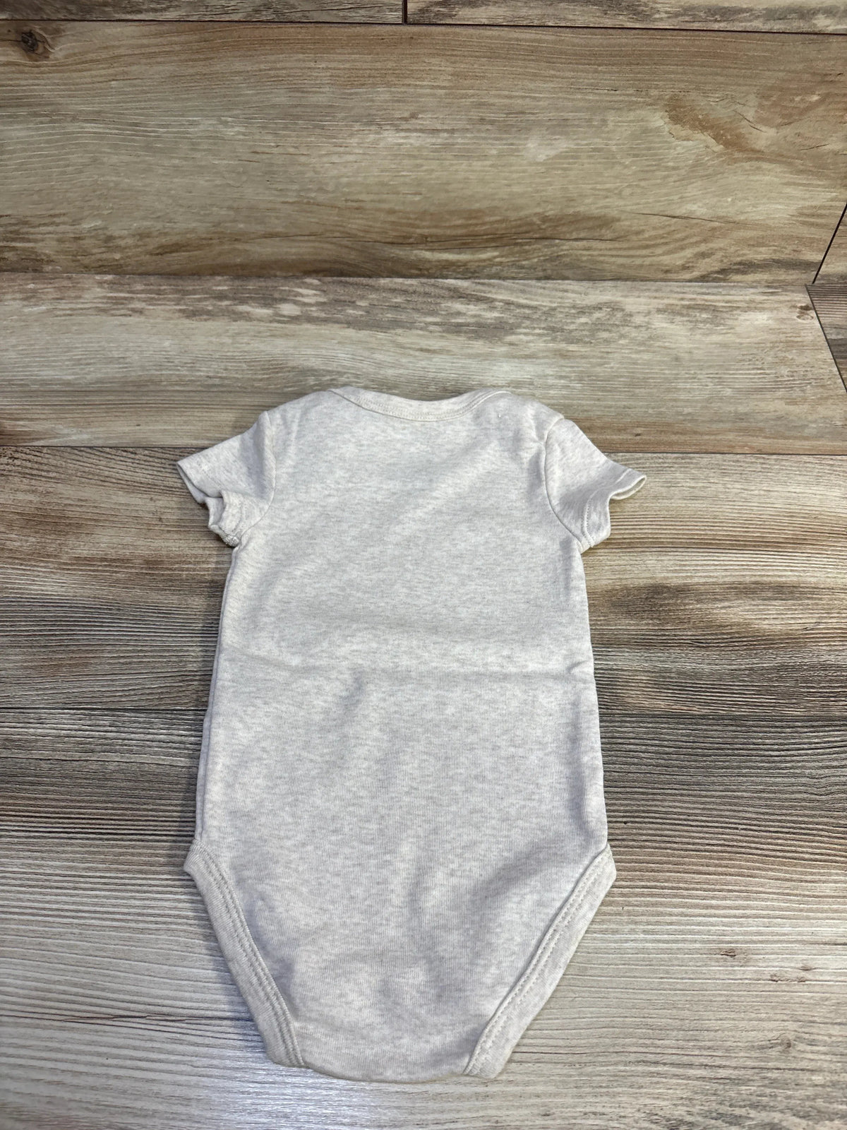 Back view of Nike beige short-sleeve bodysuit size 12M showcasing ribbed neckline and short sleeves on wood plank background