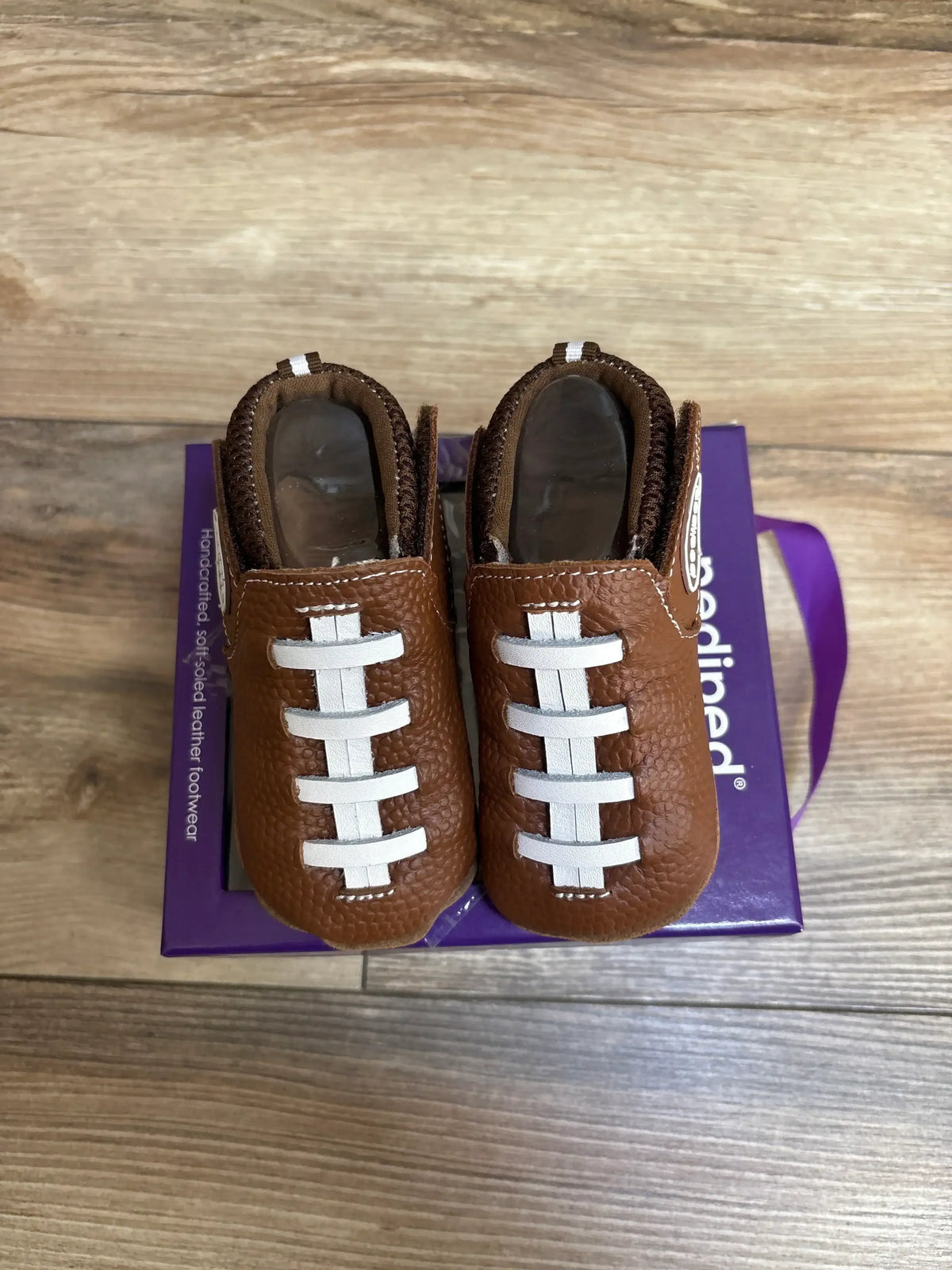 Top-down of Pediped baby shoes size 5C showing white football laces on brown leather on a purple box