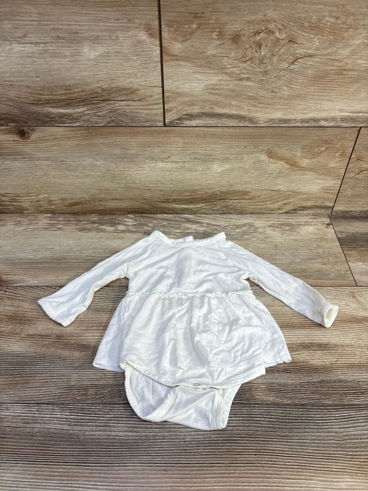 Flat lay of Spearmint Love white bamboo long-sleeve bodysuit dress with peplum skirt and snap crotch on light wood background