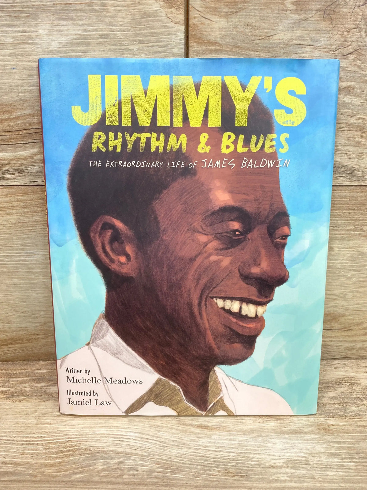 Front view of hardcover Jimmy's Rhythm and Blues with illustrated portrait of James Baldwin and bold yellow title on blue