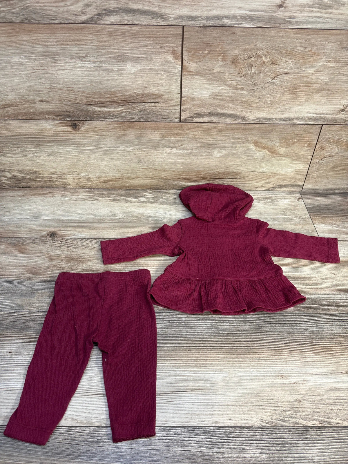 Flat lay of Carters two piece baby outfit set showcasing maroon hooded peplum top and coordinating pants on a wood look floor