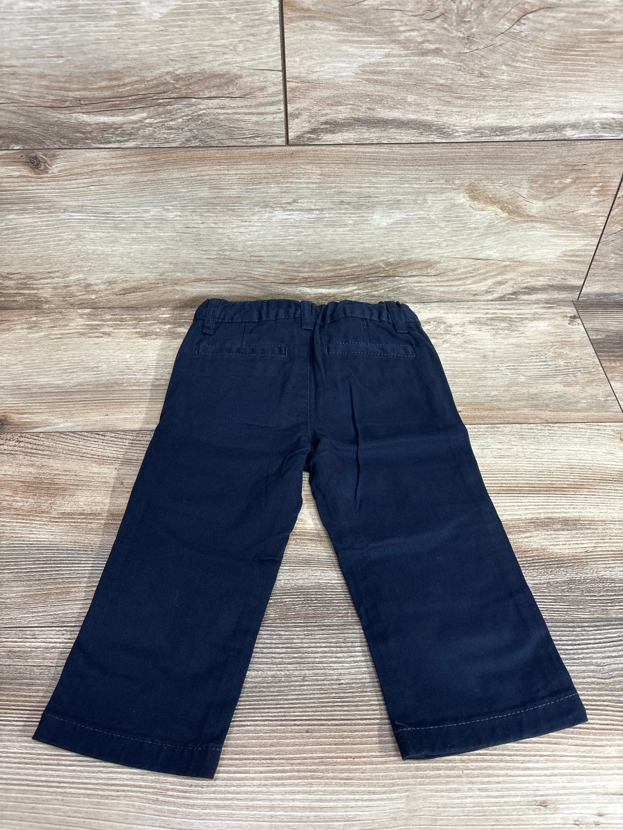 Back view of navy toddler stretch chino pants with elastic waistband and welt back pockets on light wood floor