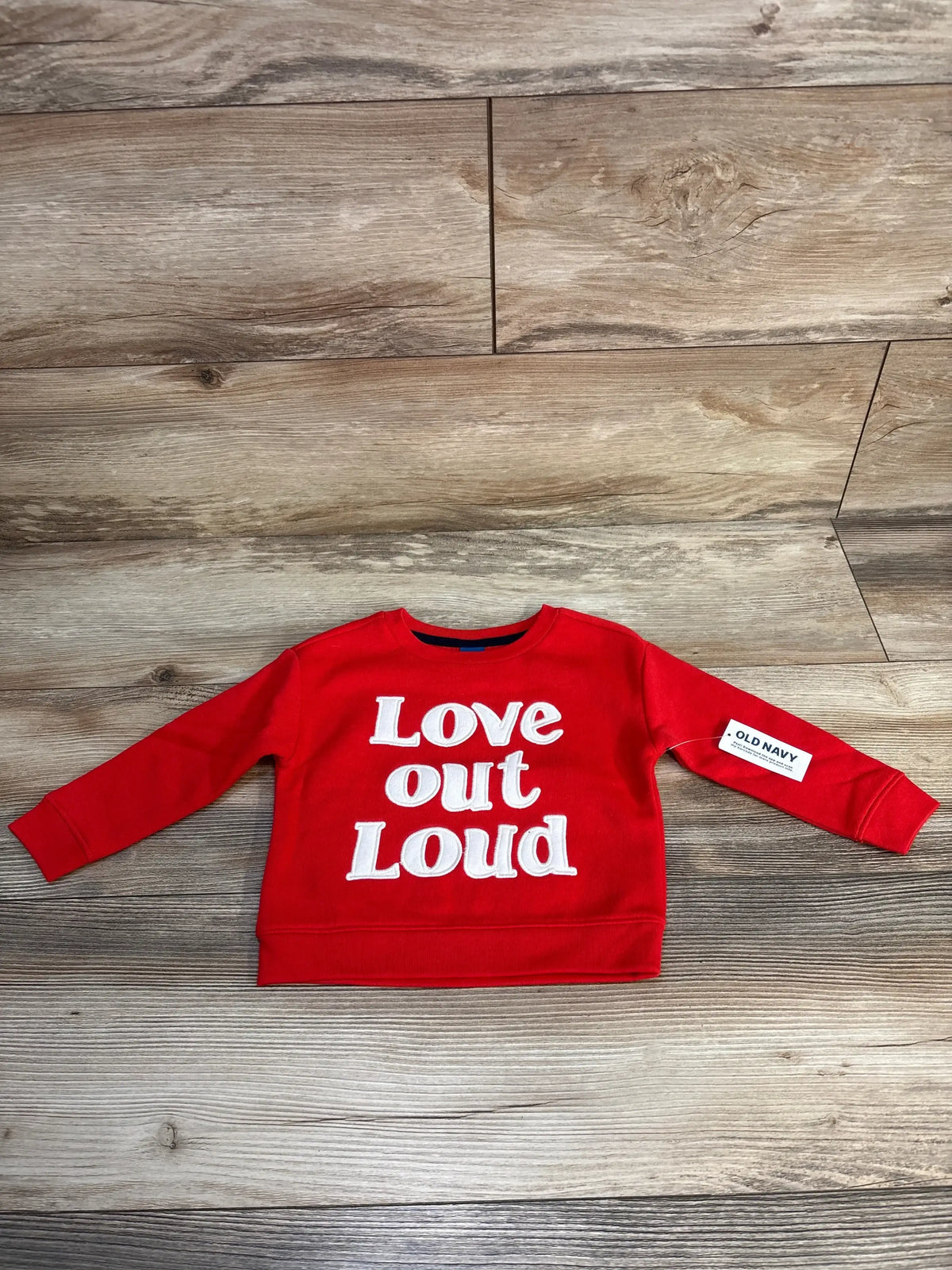 Red kids sweatshirt with 'Love out Loud' text, Old Navy tag, on wood background