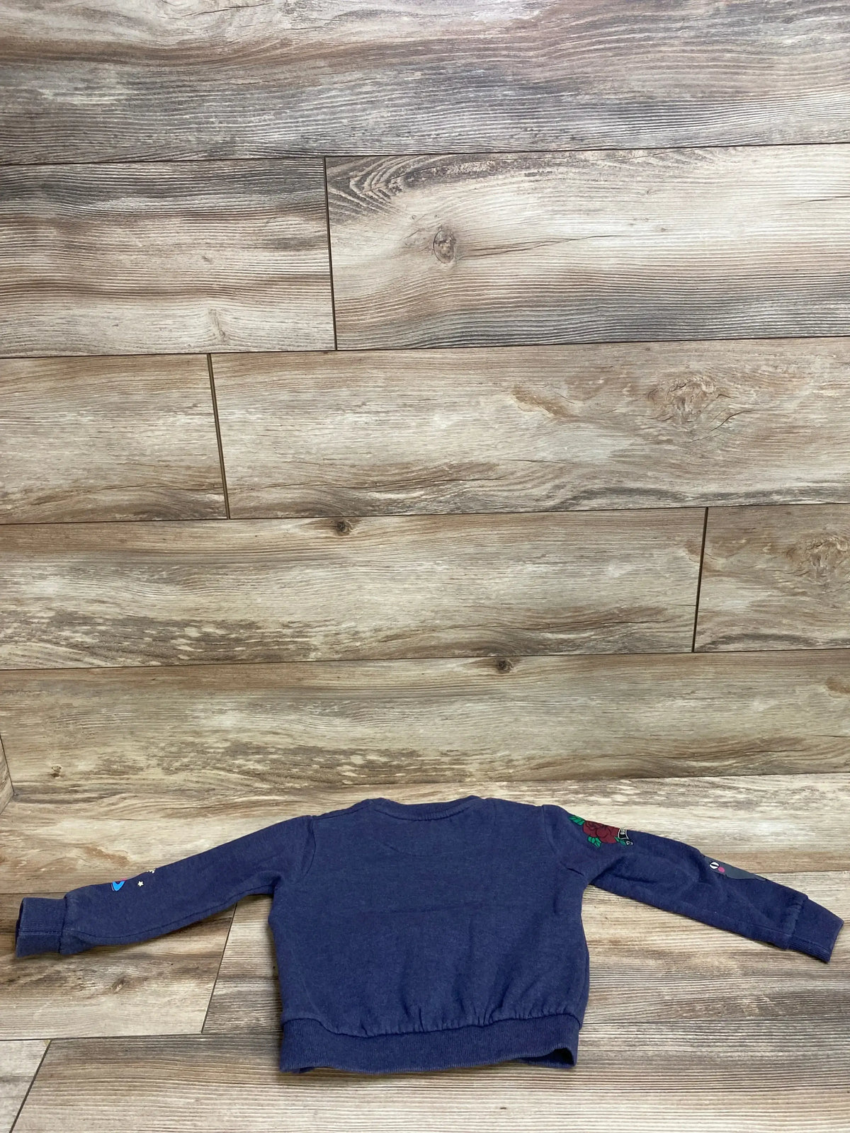 Back view of navy blue toddler sweatshirt with colorful patches on sleeves, displayed on wooden floor