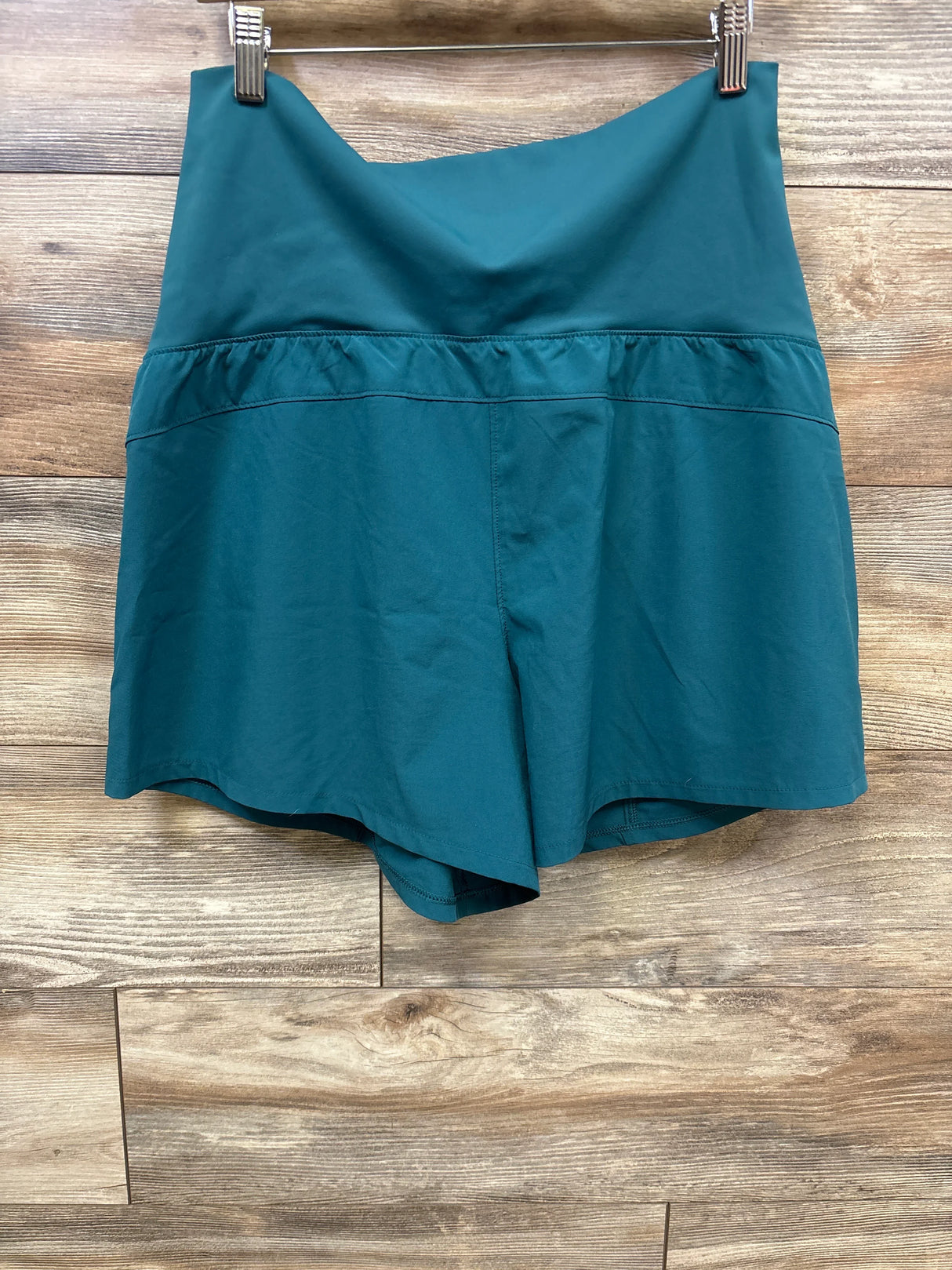 Teal maternity or activewear shorts with a wide waistband hanging on wooden background