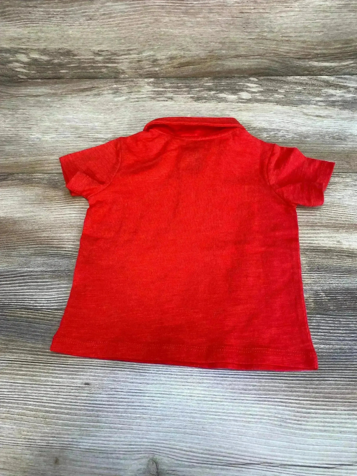 Back view of First Impressions red polo shirt, size 6-9 months, showing short sleeves and foldover collar on wood background