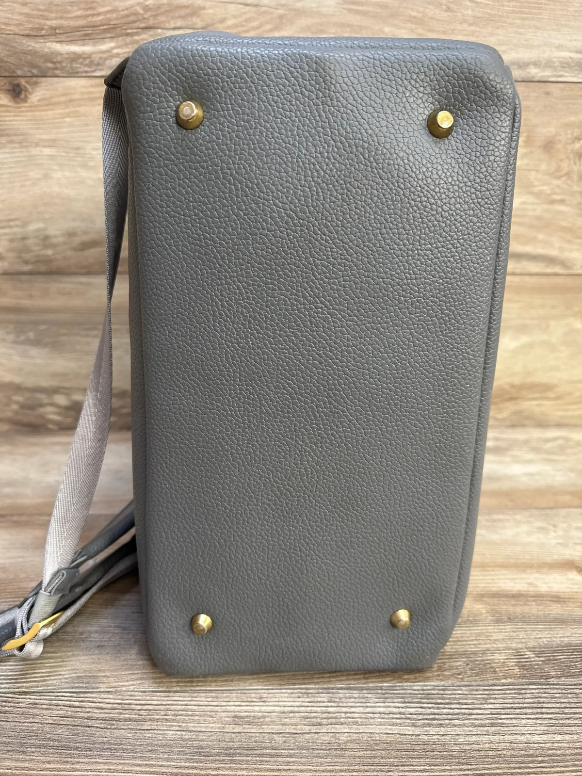 Side view of Freshly Picked Stone Classic Diaper Bag II showcasing pebble-textured base with four gold feet and strap on wooden background