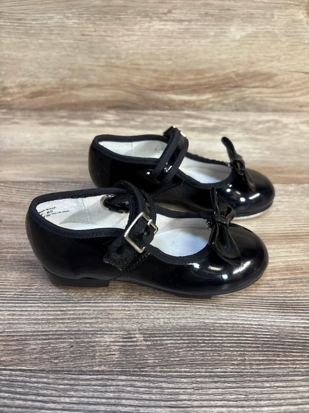 Black patent leather toddler Mary Jane shoes with bows and buckles on wood background
