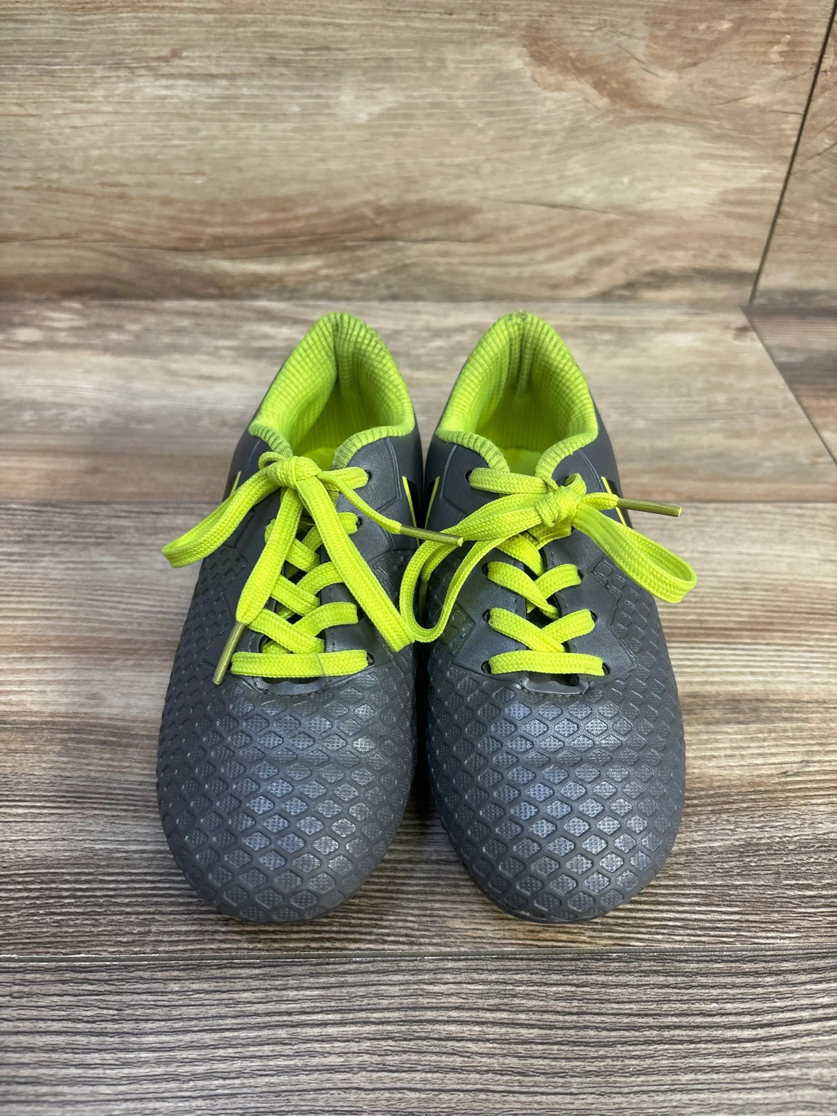 Top-down view of toddler grey Hawkwell soccer cleats with textured uppers and neon yellow laces on wood floor