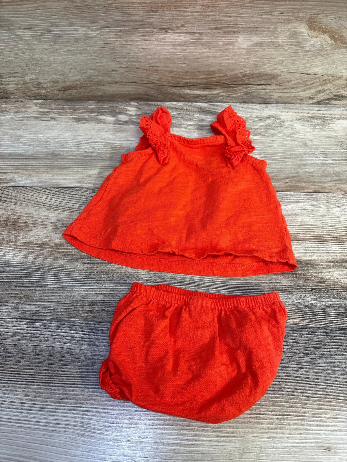 Flat lay of red Carter's baby peplum top and bloomers with ruffled eyelet straps and elastic waist on wood background