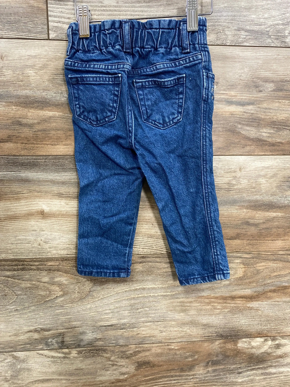Back view of Baby Gap Denim Star jeans in blue showcasing elastic waistband and two back pockets clipped to hangers on wood plank floor