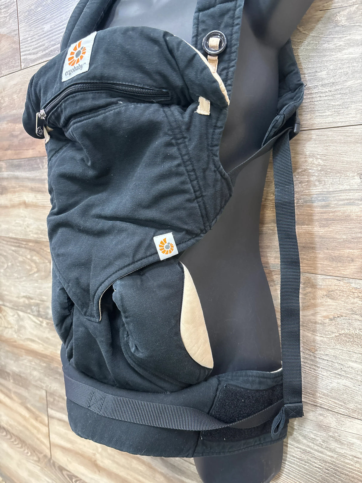 Side view of Ergobaby Four Position 360 carrier, black with tan lining, showing zippered hood pocket, padded waist belt and adjustable shoulder straps on a mannequin
