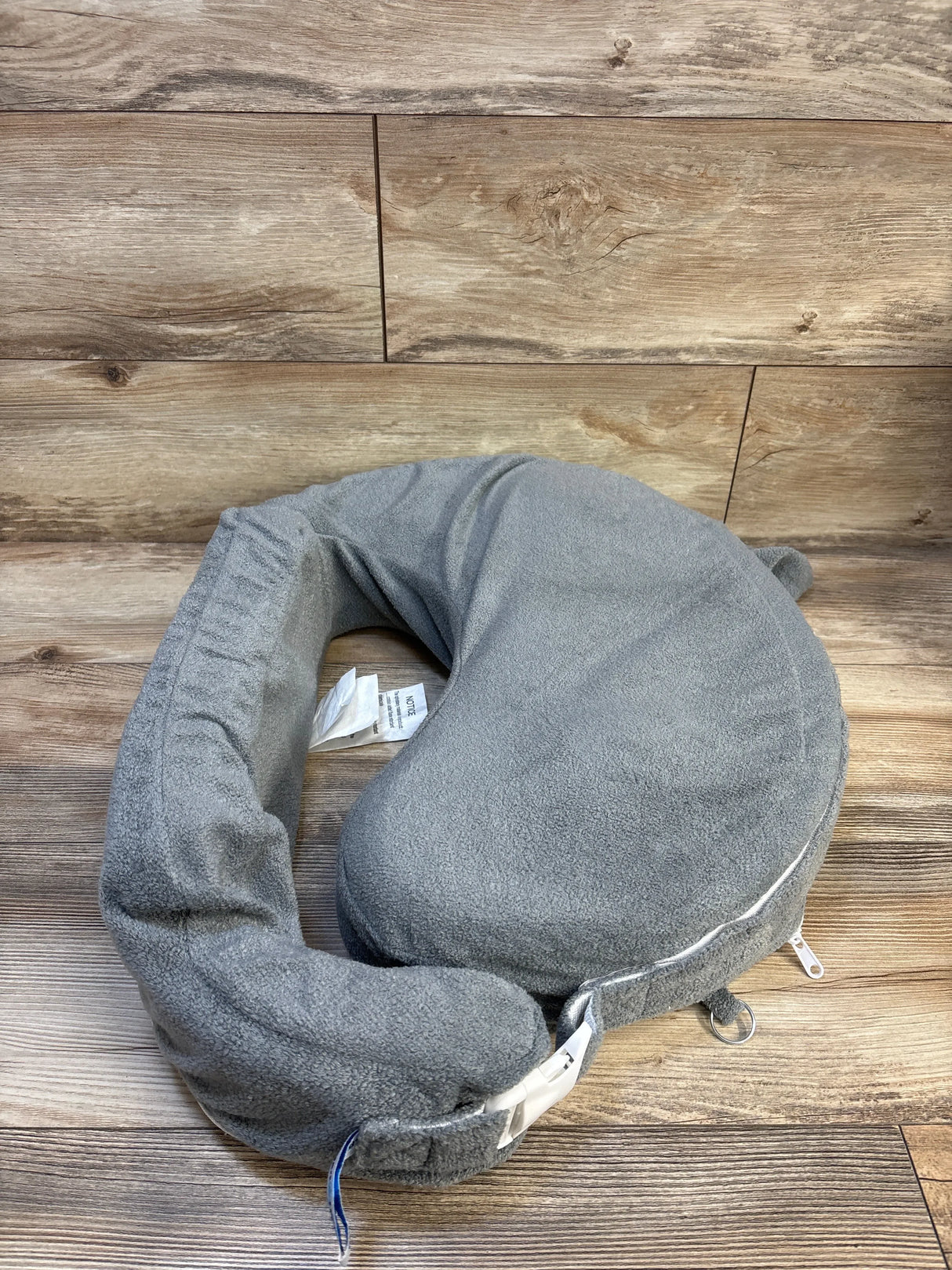 Gray nursing pillow with adjustable strap on wood background, baby feeding accessory
