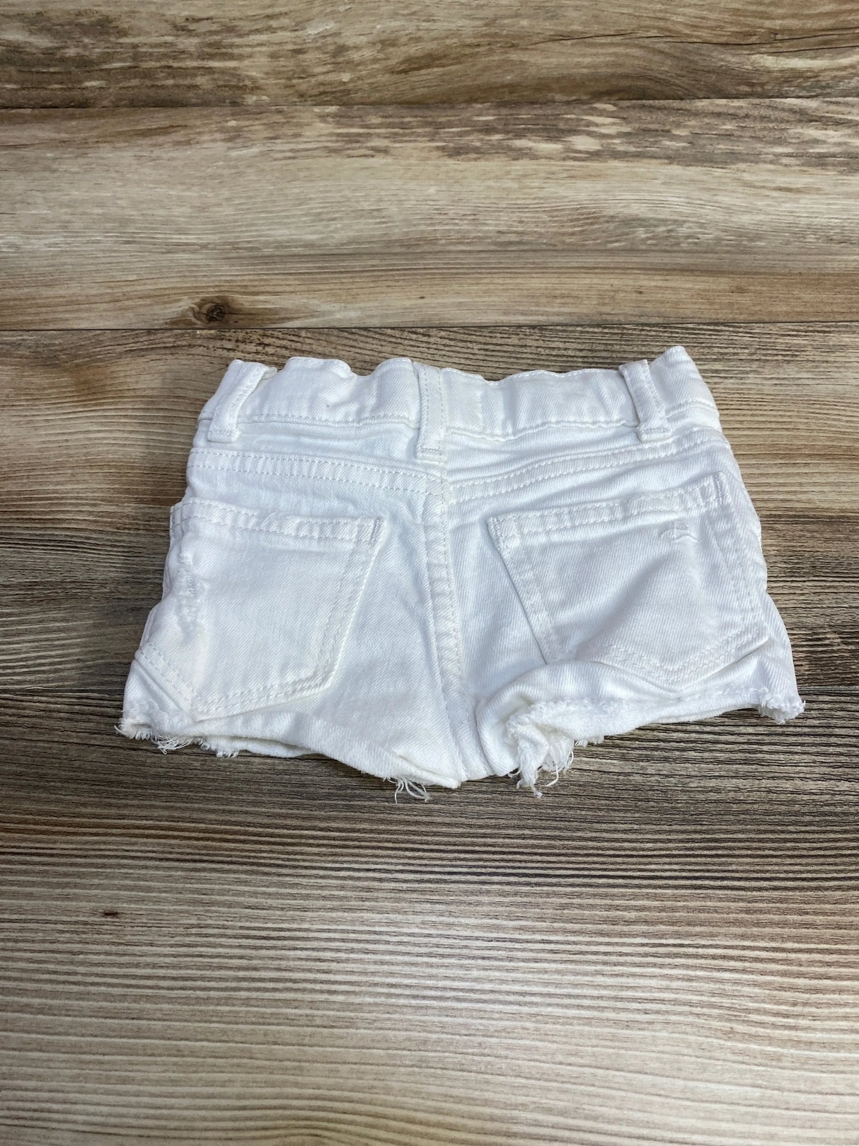 Back view of DL1961 Lucy white denim toddler shorts size 2T showing elastic waistband, back pockets, and frayed hem on wood