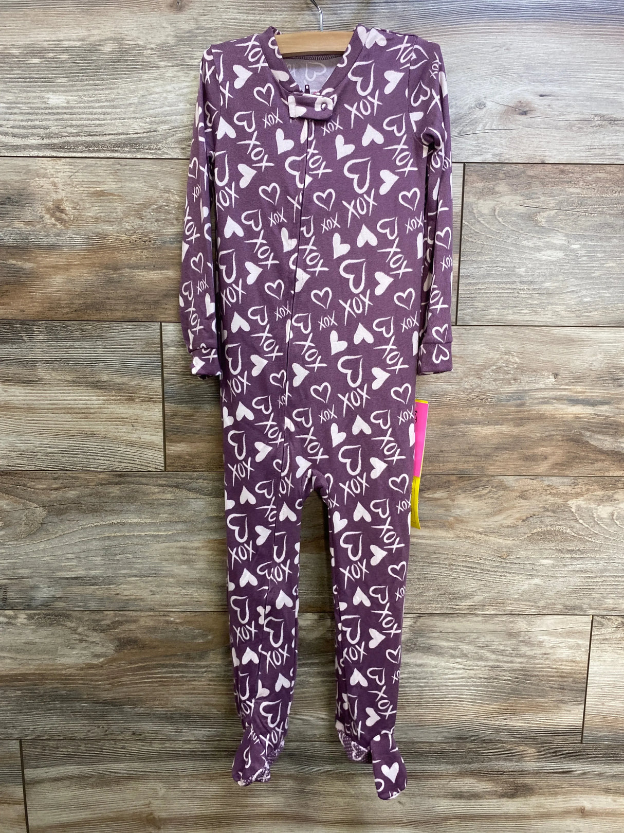 Front view of Betsey Johnson purple toddler footed sleeper (4T) showcasing all-over white XOXO and heart print with wood background