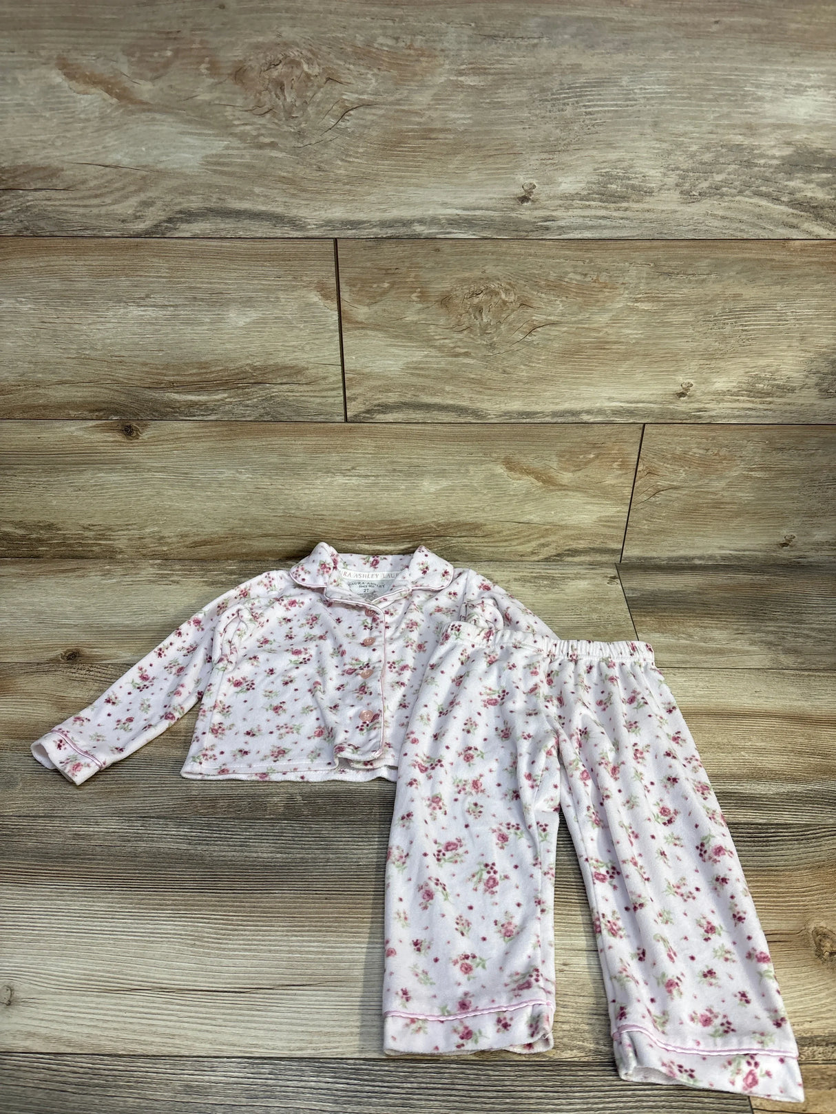 Girls pink floral pajama set with long sleeves and pants, laid flat on wood floor