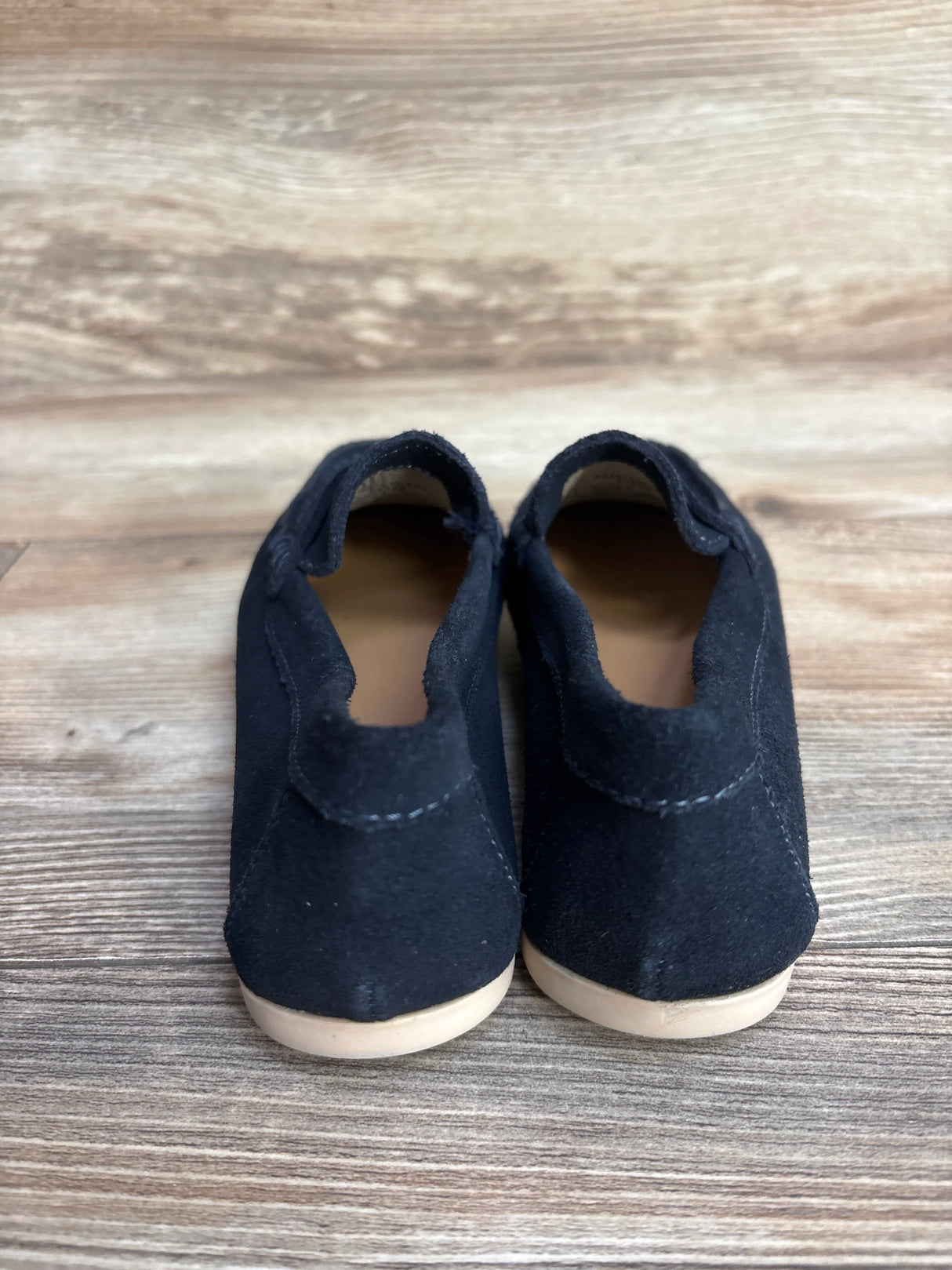 Black suede moccasins with soft soles on wood floor, toddler shoes, back view