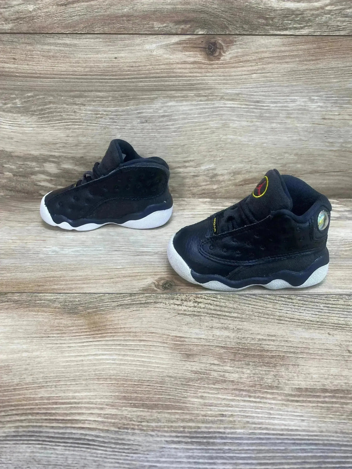 Angled view of Air Jordan 13 Playoff toddler sneakers with black upper, white sole and hologram heel on wood background