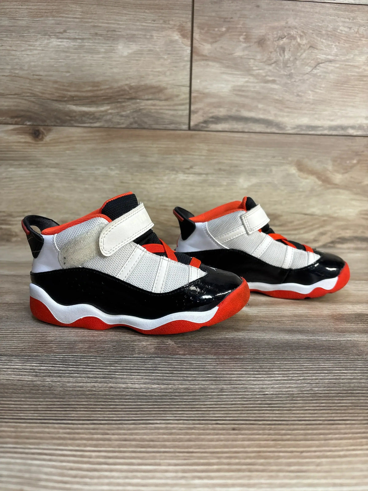 Kids' black, white, and orange high-top sneakers with velcro straps on wooden floor