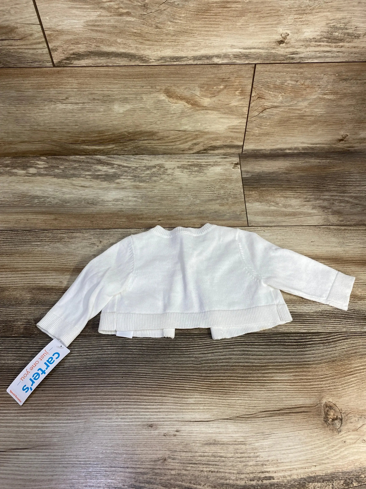 White Carters baby cardigan with long sleeves on wood texture background