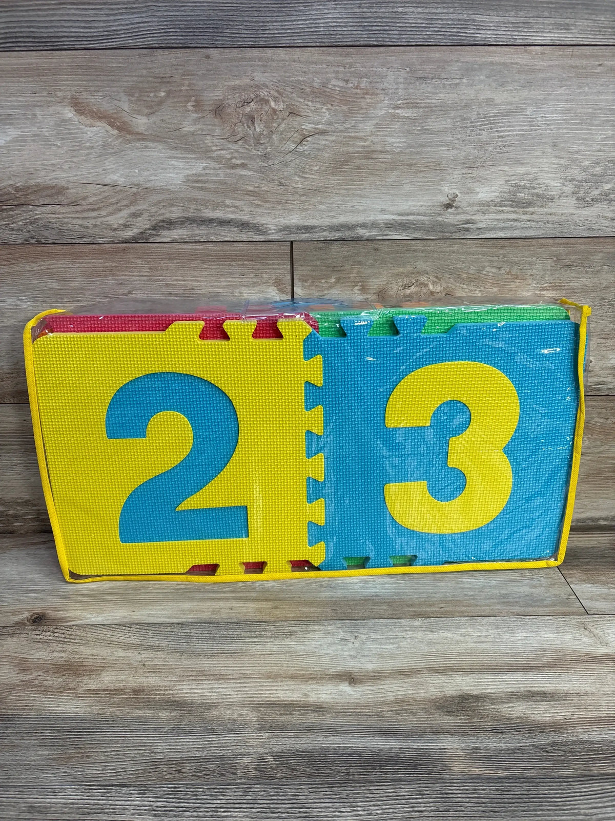 Front view of Lakeshore heavy-duty hopscotch puzzle mats showing blue 2 and yellow 3 foam tiles in clear zip case on wood floor