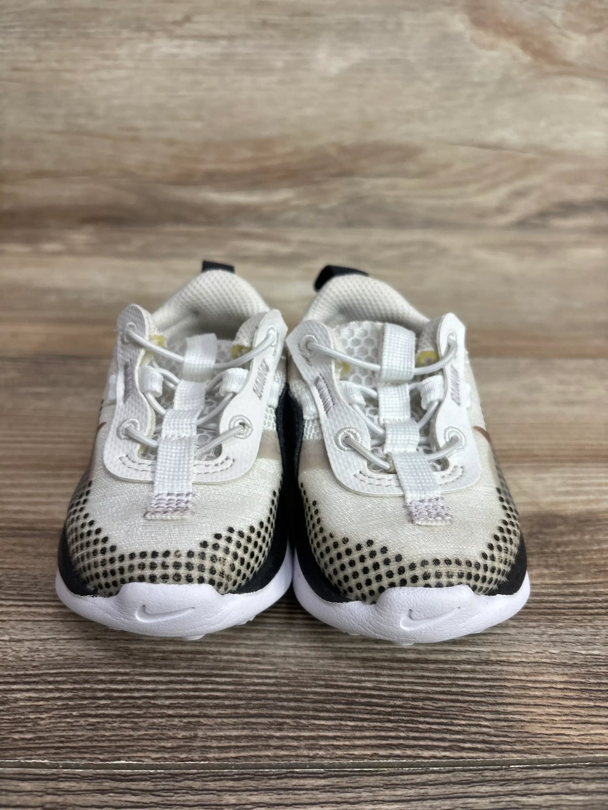 Front view of toddler Nike Air Max 2021 shoes showing white mesh uppers, black dotted toes, elastic bungee laces on wood background