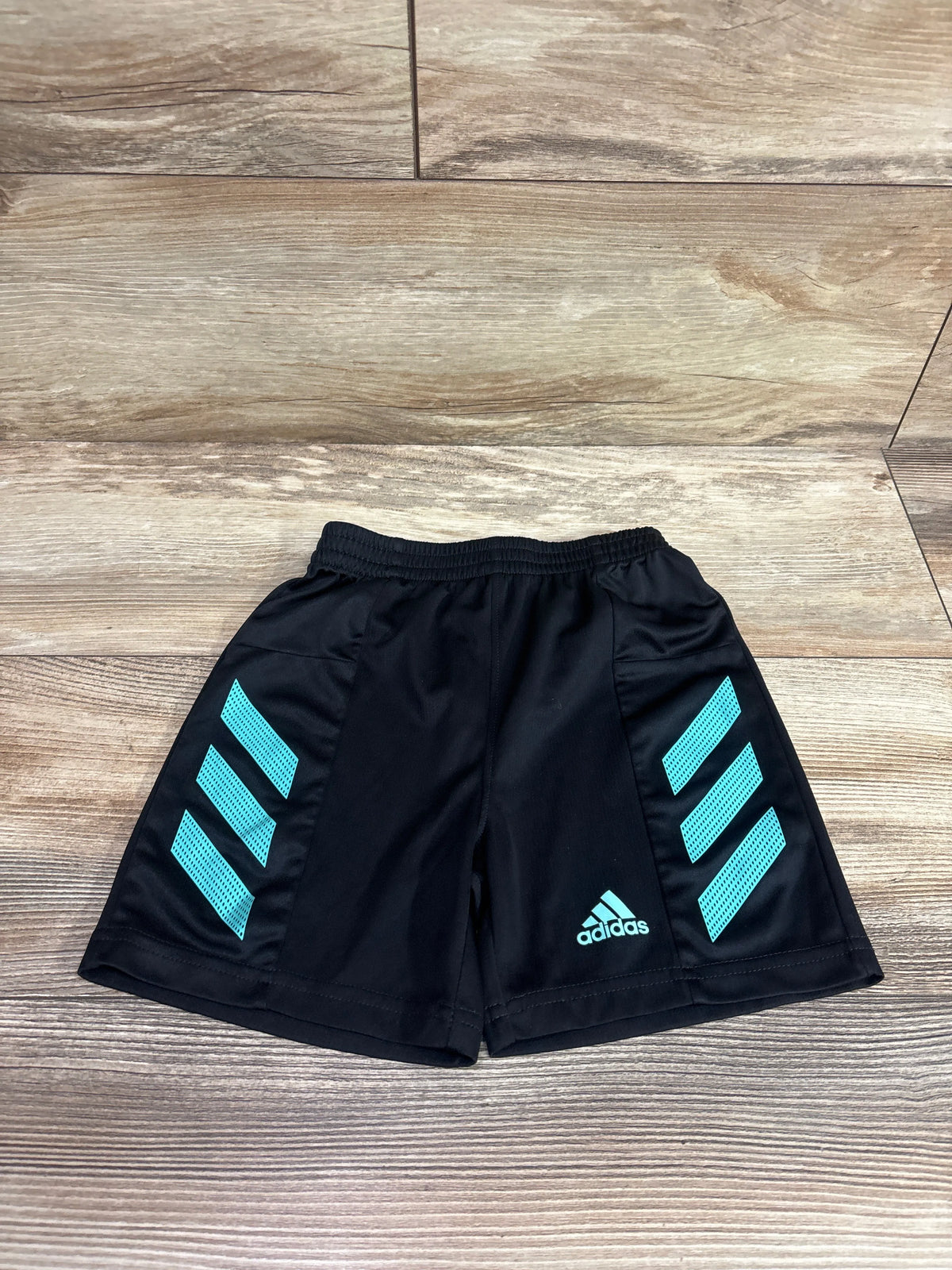Front view of black Adidas mesh shorts showcasing turquoise side stripes and elastic waistband on a wood floor