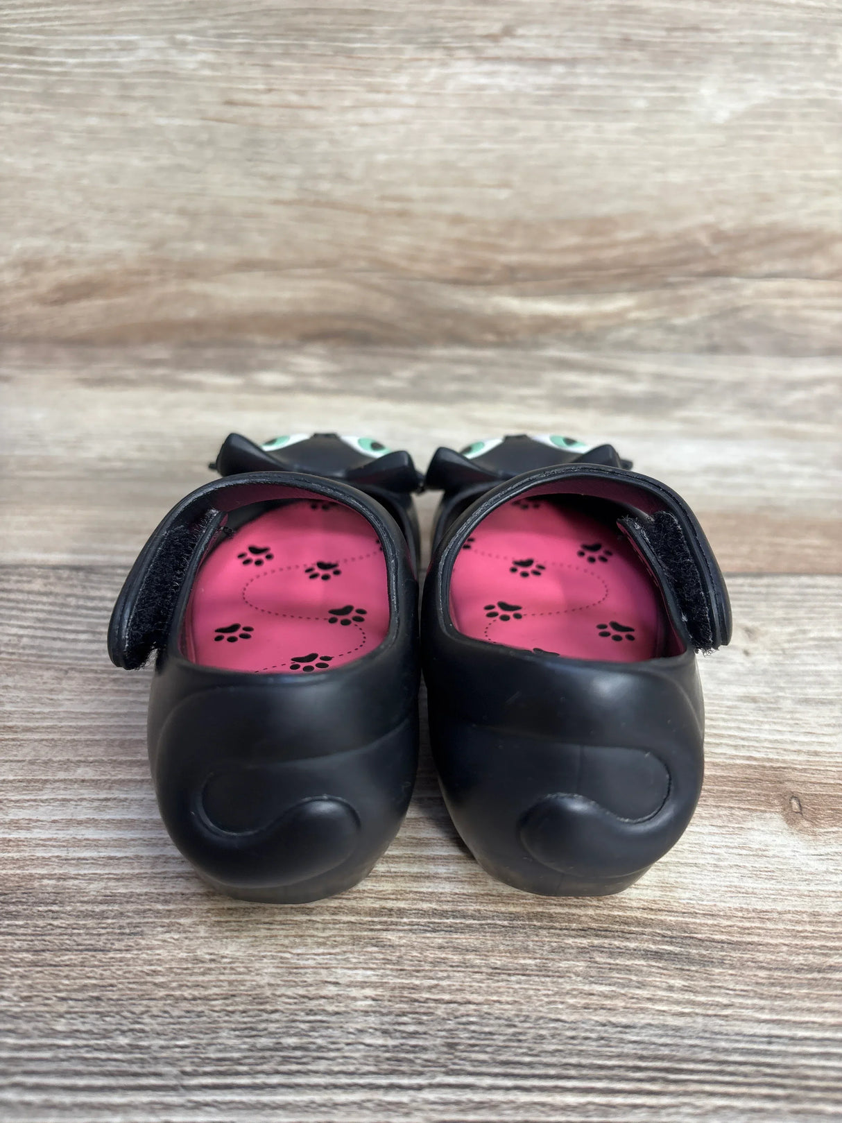 Front view of Mini Melissa Ultragirl II Cat jelly flats size 7C showcasing black cat-face toes and pink insoles with paw-print pattern on wooden floor