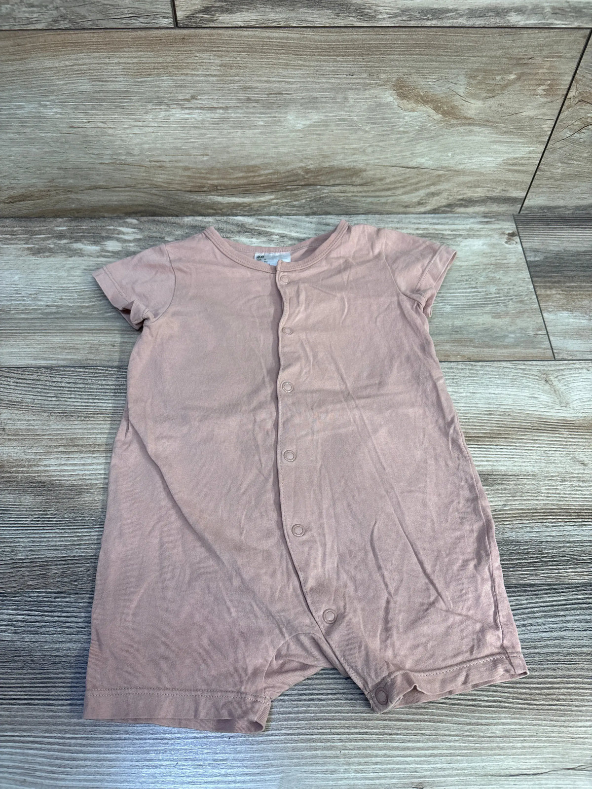 Front view of H&M tan button-front shortie romper showcasing short sleeves and snap closures on a wood-look floor