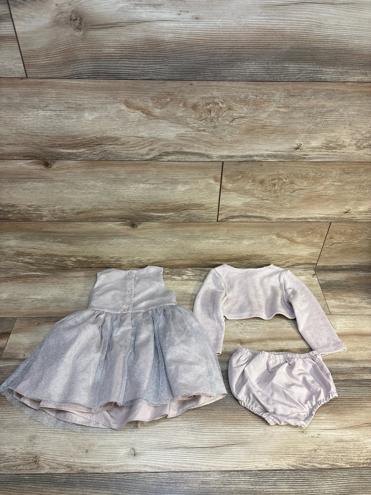 Front view of Pippa & Julie pink three-piece dress, bloomers, and cardigan set showcasing metallic fabric on a wood floor