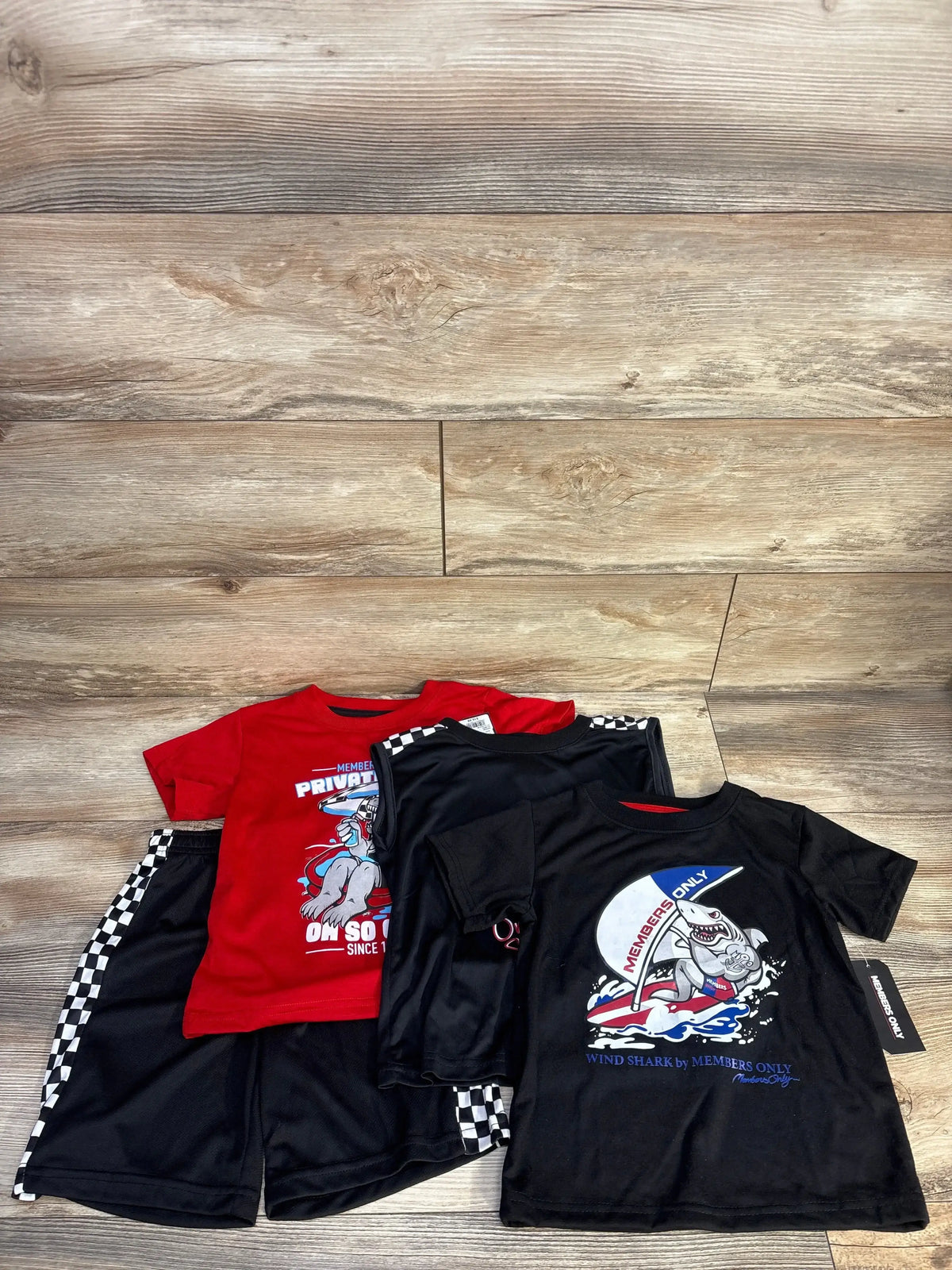 Top view of Member’s Only 4-piece set showing two short-sleeve shirts, a tank top, and checkerboard-striped mesh shorts on wood flooring