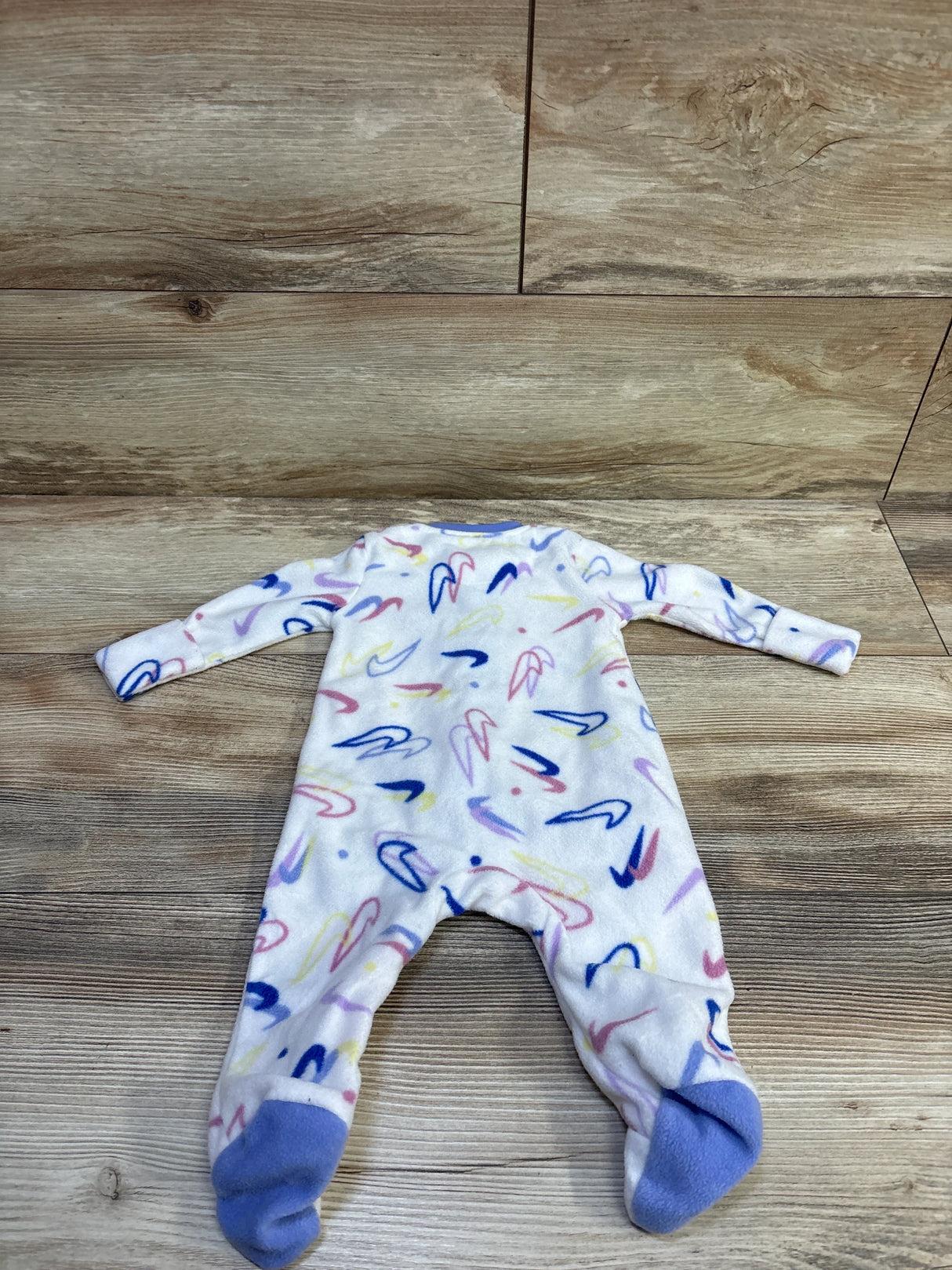 Flat lay of white Nike blanket sleeper (size 3M) with pastel multicolor swoosh print, long sleeves and footed design on wood background