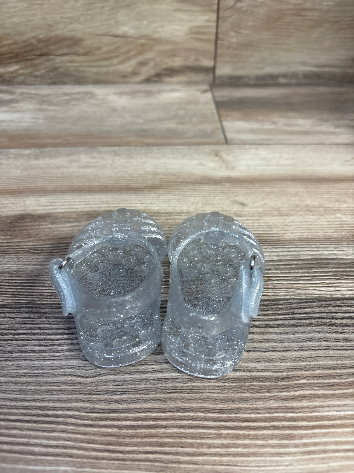 Top-down view of toddler jelly sandals (size 1C) showcasing clear glitter and ankle strap on wood floor