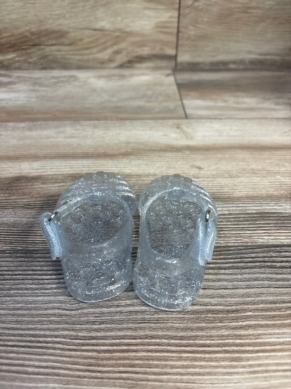 Top-down view of toddler jelly sandals (size 1C) showcasing clear glitter and ankle strap on wood floor