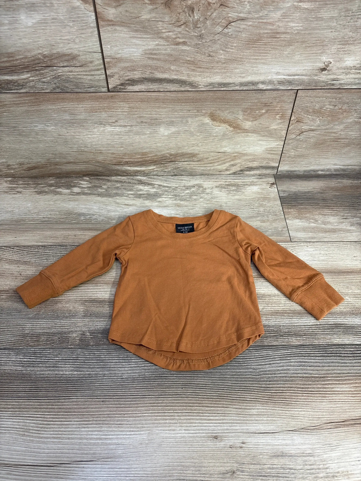 Rust brown long sleeve toddler shirt with curved hem on wood background