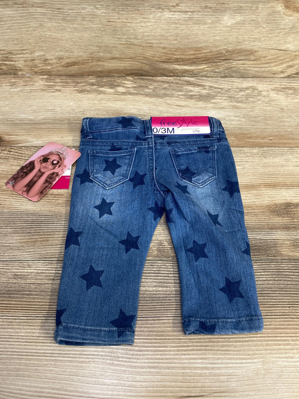 Back view of newborn blue star print jeans showing two back pockets, rolled hems and size 0-3M tag on wood background