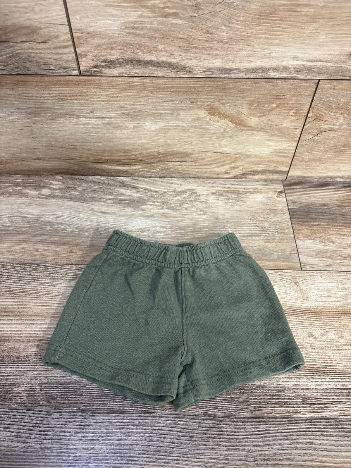 Front view of Carters green pull on shorts in size 12 months showcasing elastic waistband with wood look floor background